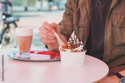 Hands of man eating frozen yogurt at cafe table