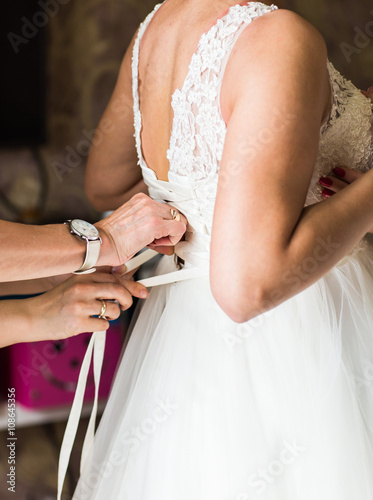 Bridesmaid is helping the bride to dress