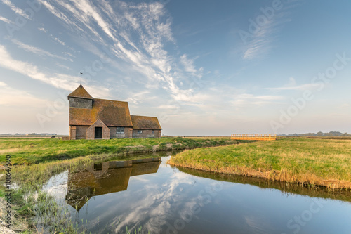 Thomas Becket church, Fairfield, Romney Marsh reflected in river water.