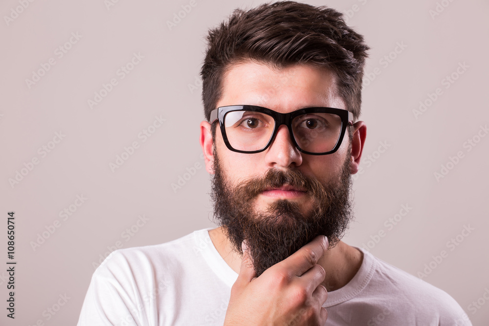 Face portrait of bearded man in glasses with hand on beard against white background