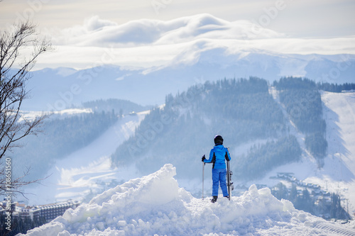 Rear view of girl skier standing on top of the mountain and enjoying the view on beautiful winter mountains on a sunny day. Winter sports concept. Bukovel