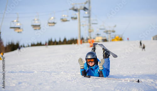 Young happy skier woman in blue ski suit orange goggles and helmet lying on the snow on a sunny day. Ski vacation. Ski resort at Carpathian Mountains, Bukovel, Ukraine