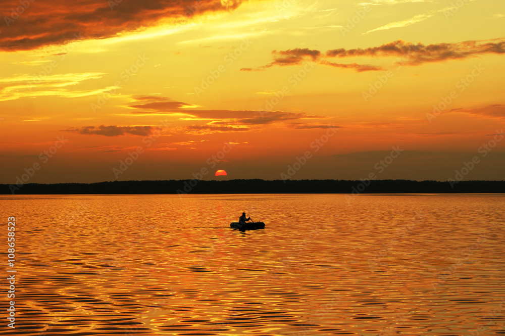 Lonely boat floating on the lake during sunset. Fisherman catches a fish.