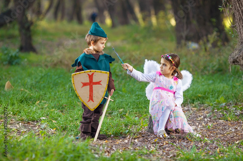 Cute little children dressed up as a fairy and a knight playing in a forest