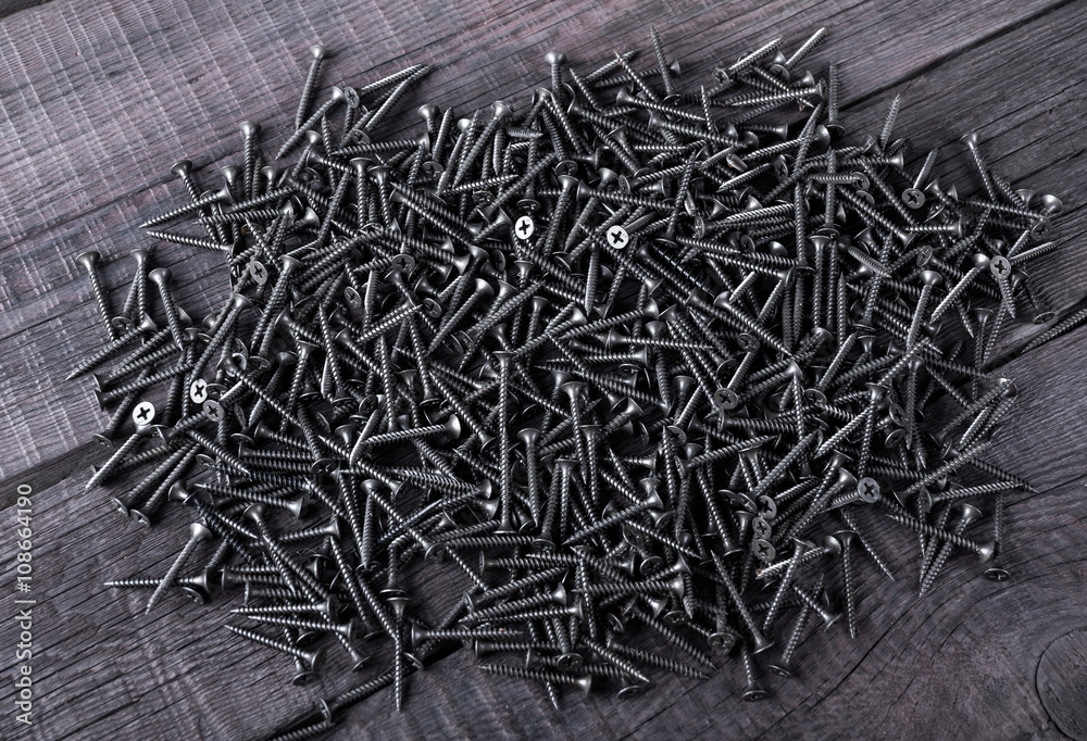 Pile of black screws on wooden background