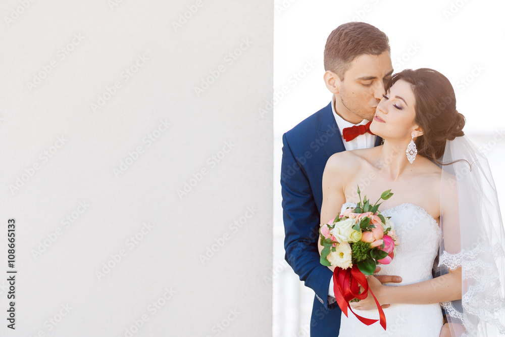 Young wedding couple kissing near a gray wall Young wedding couple kissing near a gray wall