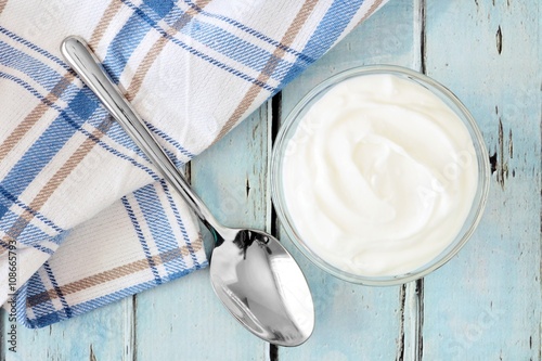 Greek yogurt in a bowl, downward view with cloth and spoon on a rustic soft blue wood background
