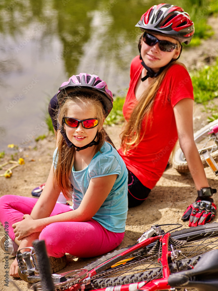 Naklejka premium Bikes cycling family. Happy mother and daughter rides bicycle. Family have rest near water in park. Bicycles are on coast. Active outdoor recreation.