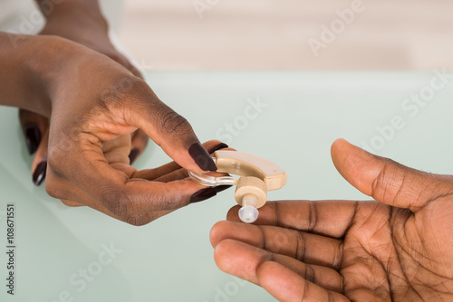 Doctor's Hand Giving Hearing Aid To Patient