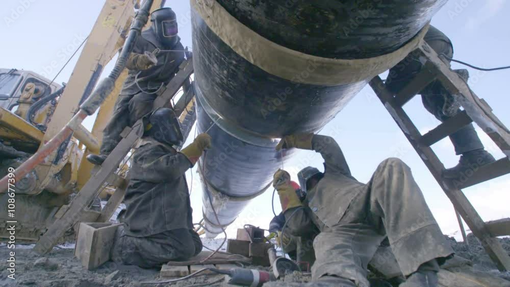 Industrial workers welding steel duct pipe by using metal torch in sunny winter day