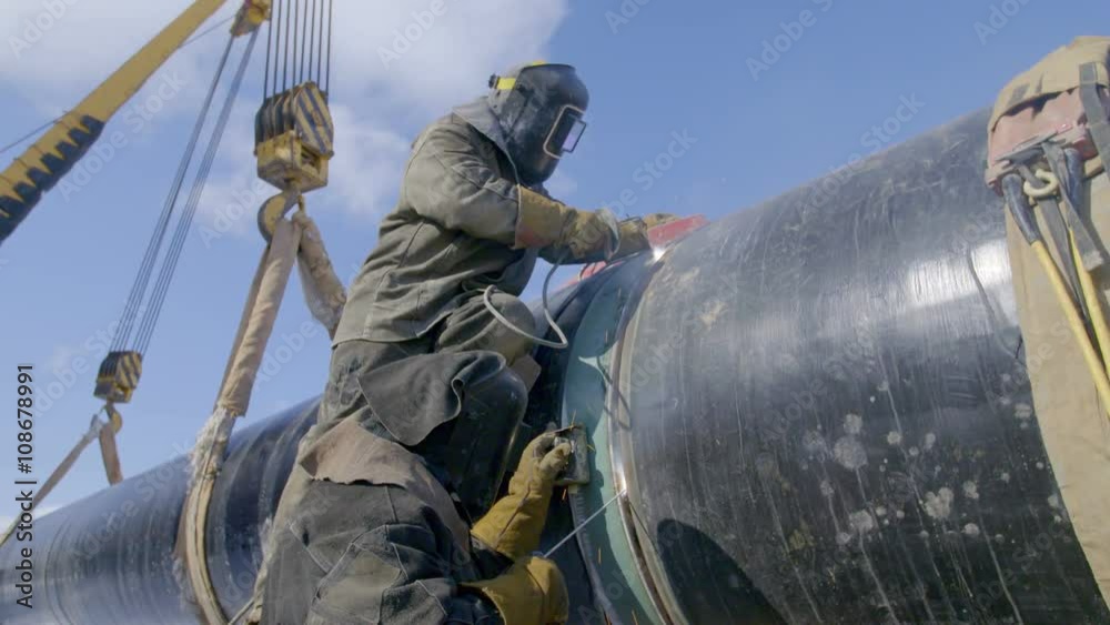 Industrial workers welding steel duct pipe by using metal torch in sunny winter day