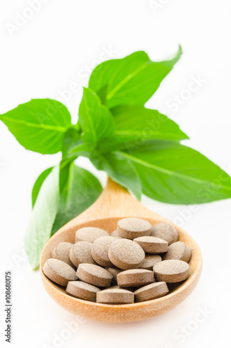 Herbal tablets in wooden spoon with green leaf.