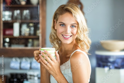 Happy young woman holding coffee cup at home