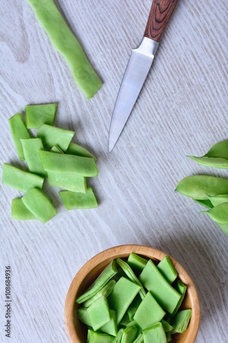 Green peas, knife and wooden bowl on table