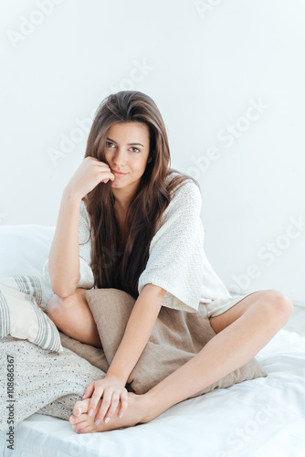 Tender cute young woman sitting on bed