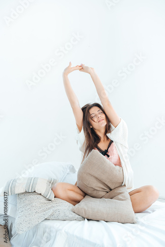 Relaxed woman sitting and stretching on bed