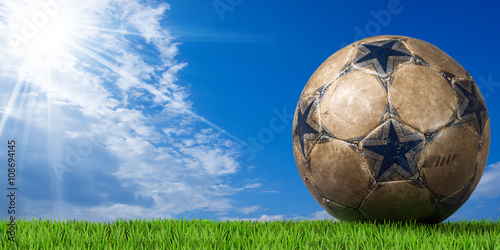 Blue and brown soccer ball  Football  with green grass and blue sky with clouds and sun rays