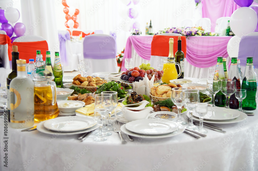 Interior festive Banquet hall for the newlyweds with round tables. Table setting dishes of food and Cutlery. The Banquet design. Decorated Banquet hall for guests. Interior festive Banquet hall for the newlyweds with round tables. Table setting dishes of food and Cutlery. The Banquet design. Decorated Banquet hall for guests.