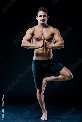 Sporty fit young athlete sportswear working out, holding palms in Namaste gesture, studio black background