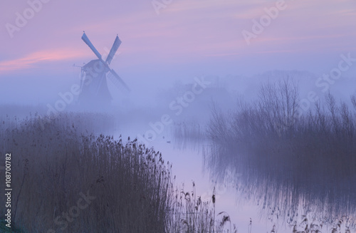 Foggy, pink sunrise in Holland with a traditional windmill in the wetlands.
