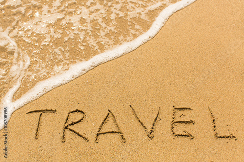 Travel - inscription by hand on yellow beach sand.