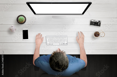 Man work on computer with white isolated screen. Work desk with plant, camera, coffee, smart phone. Top view.