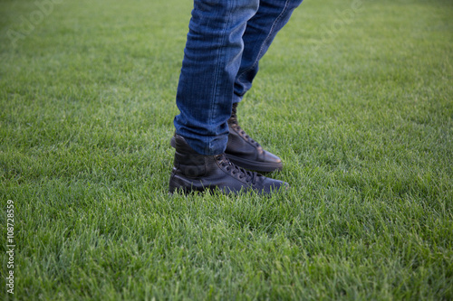 Leg of a man with Blue Jeans and Black Shoes is walking on the Meadow