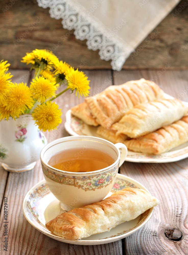 Pies of puff pastry with a cup of tea on a wooden table. Vintage style. Pies of puff pastry with a cup of tea on a wooden table. Vintage style.