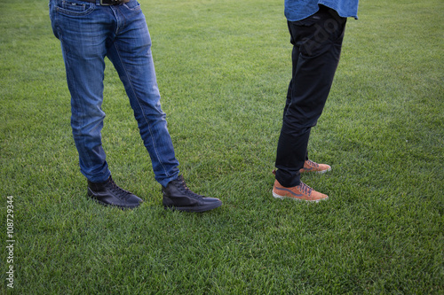Legs of two men with blue jeans and black trousers on a Green Meadow