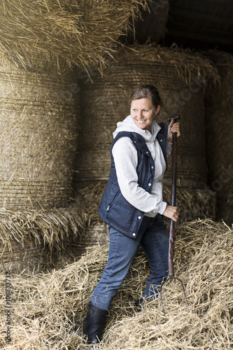Smiling woman moving hay with pitchfork