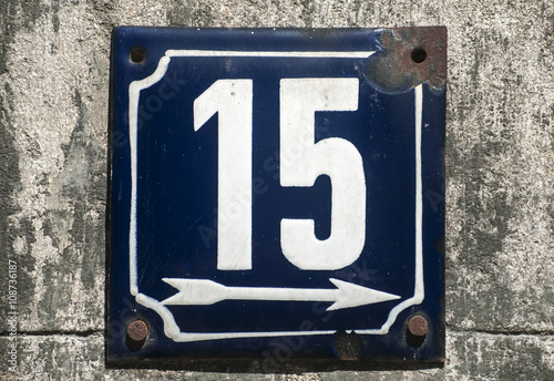 Weathered grunge square metal enameled plate of number of street address with number 15 closeup