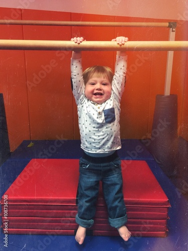 baby in gym on gymnastic bar trying to do pullup and is hanging