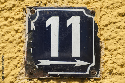 Weathered grunge square metal enameled plate of number of street address with number 11 closeup