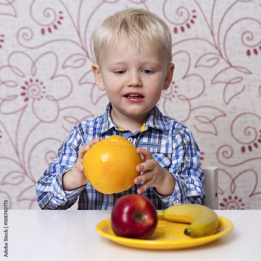 Fototapeta premium The three-year boy eats a yellow grapefruit