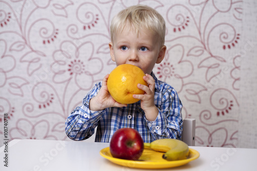 The three-year boy eats a yellow grapefruit photo