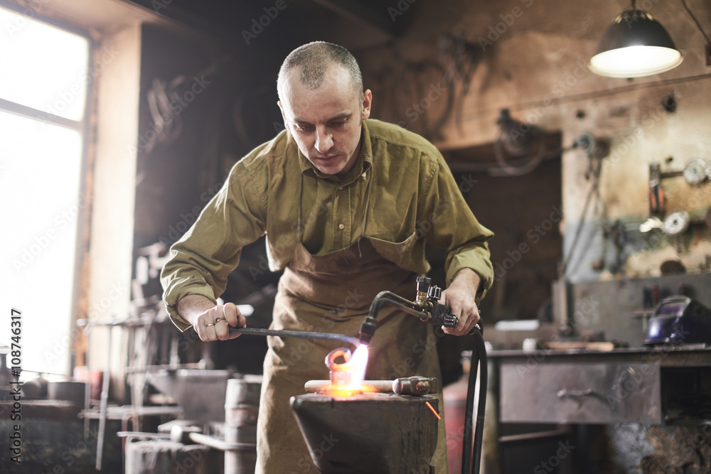 The blacksmith heats the gas burner the metal product on the anvil The blacksmith heats the gas burner the metal product on the anvil