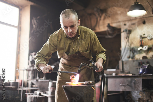 The blacksmith heats the gas burner the metal product on the anvil