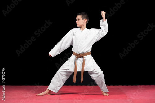 Karate boy in white kimono fighting isolated on black background