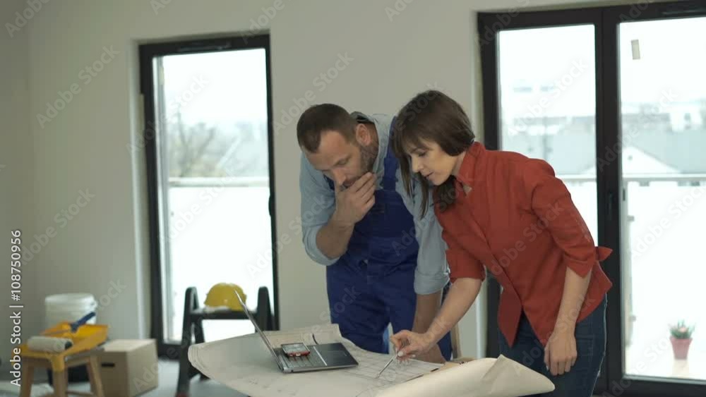 Woman and male worker talking and working with blueprints at her new home
