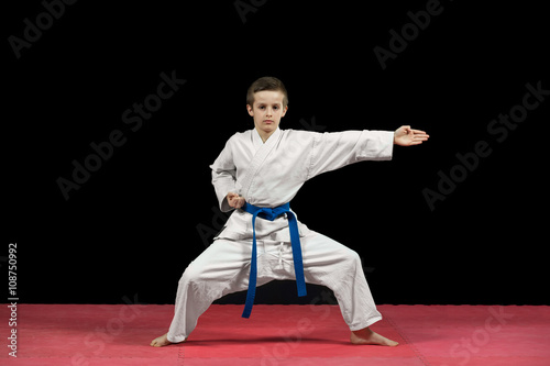 Portrait of a karate kid in kimono ready to fight isolated on black background