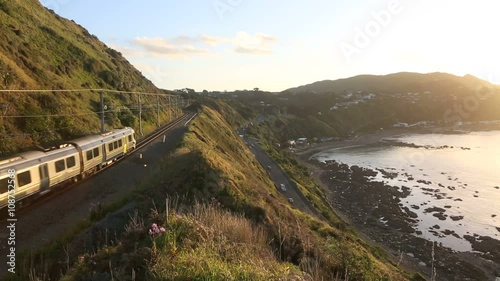 Metro commuter train and traffic at sunset on scenic highway along Kapiti coast, New Zealand 
