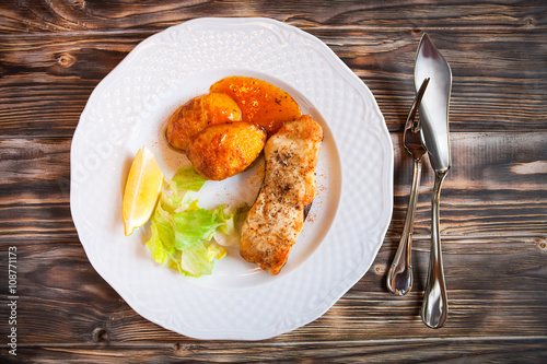 Grilled fish with potatoes, slice of lemon and red sause on wood