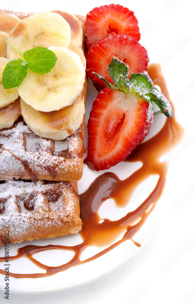 Sweet dessert:waffles with banana slices and strawberries and chocolate topping on a white background. Sweet dessert:waffles with banana slices and strawberries and chocolate topping on a white background.