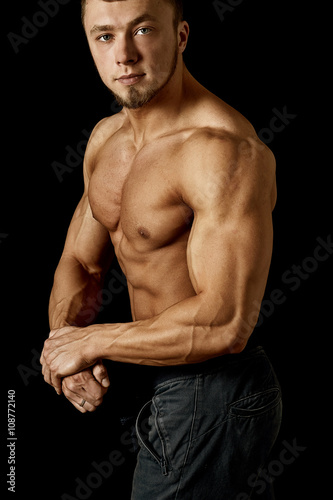 young muscular man showing his body on a dark background