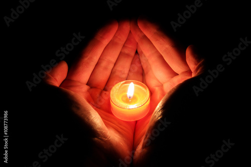 Orange burning candle in male hands. A black mirror background.