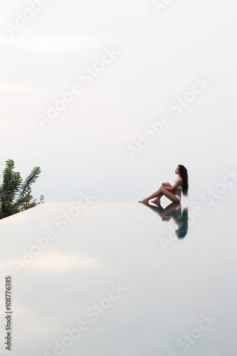 Young slim woman posing on the edge of luxury infinity pool