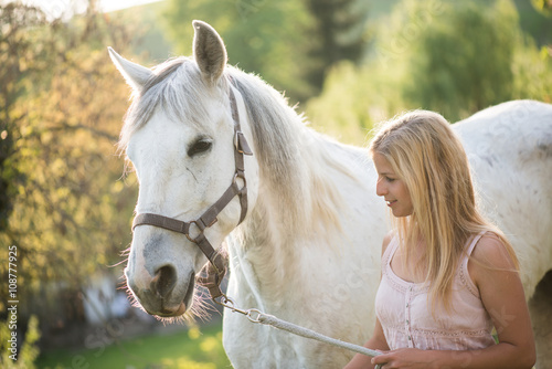 Young blonde woman posing outdoor with white horse. 