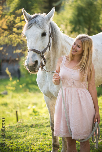 Young blonde woman posing outdoor with white horse. 