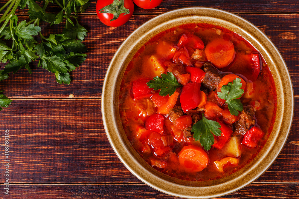 Goulash or stew in bowl served with parsley on wooden background Goulash or stew in bowl served with parsley on wooden background