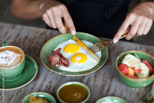 Woman cutting fried eggs with golden fork and knife at breakfast